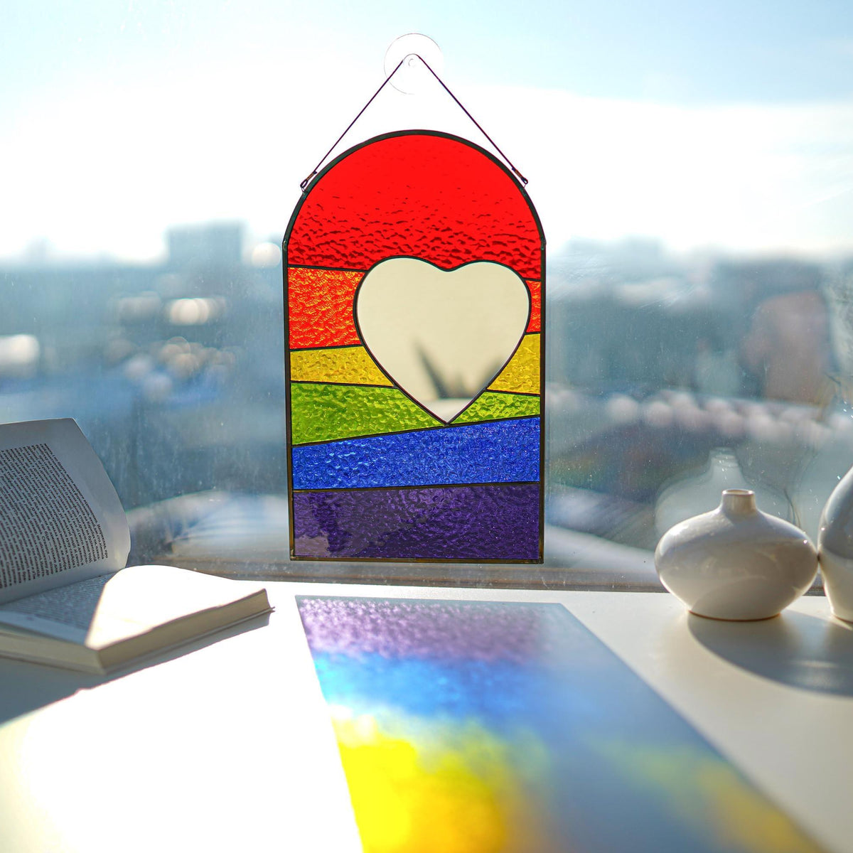 Stained glass rainbow heart suncatcher on windowsill casting rainbow reflections, mirror heart center, LGBT pride decor, 12.5x7.5 in
