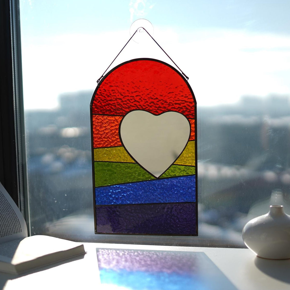 Rainbow stained glass heart panel hanging in window with colorful light reflections on table, LGBT pride gift, Tiffany style wall art
