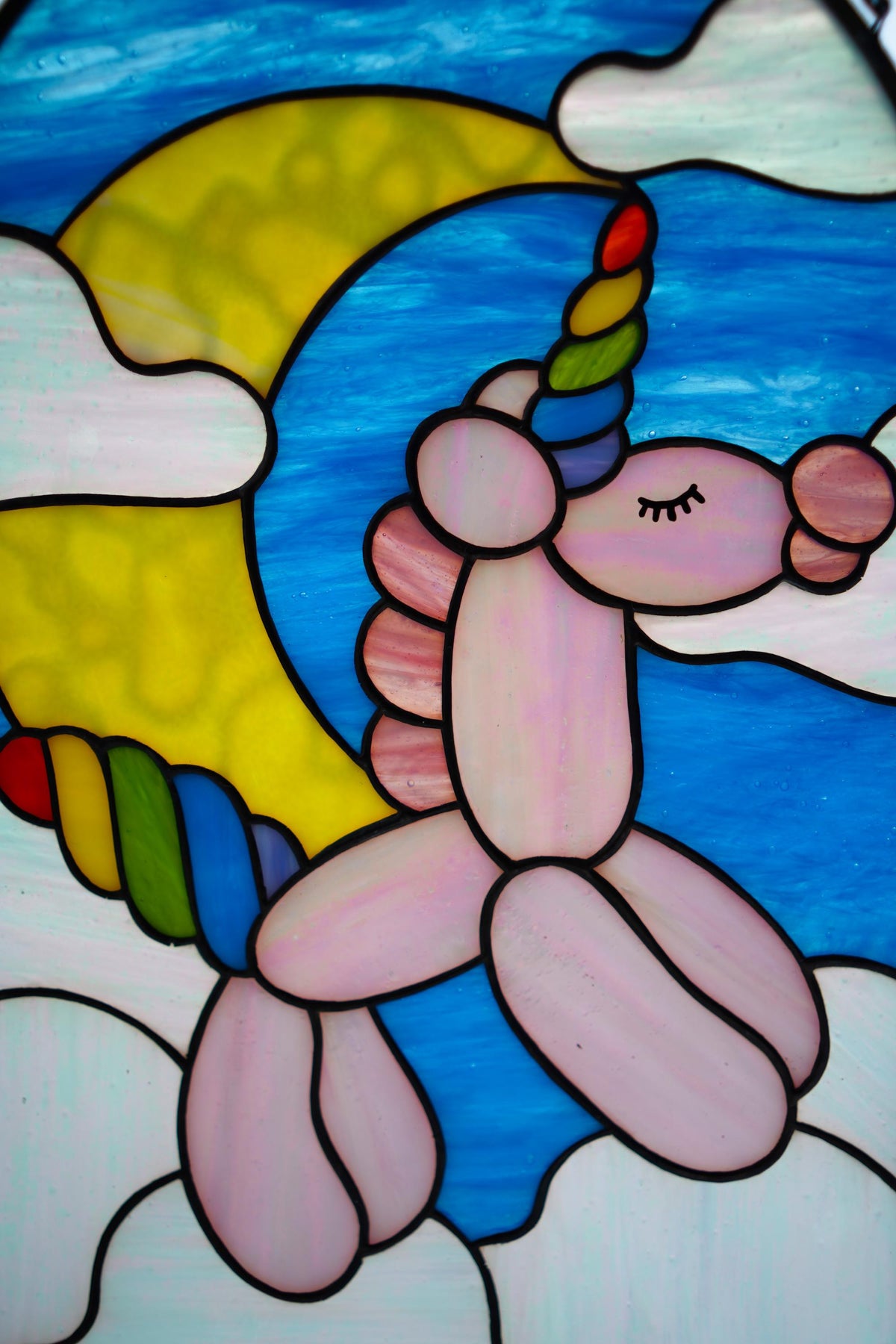 Close-up of handmade stained glass balloon unicorn, pink opalescent glass and rainbow cathedral glass details