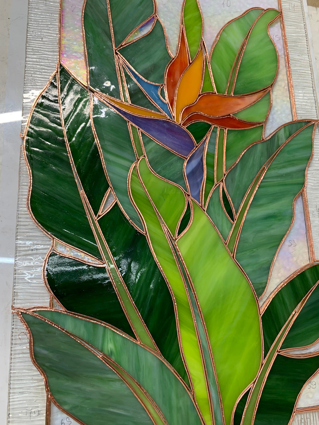 Handmade Bird of Paradise stained glass panel during assembly, orange and green cathedral glass pieces laid out