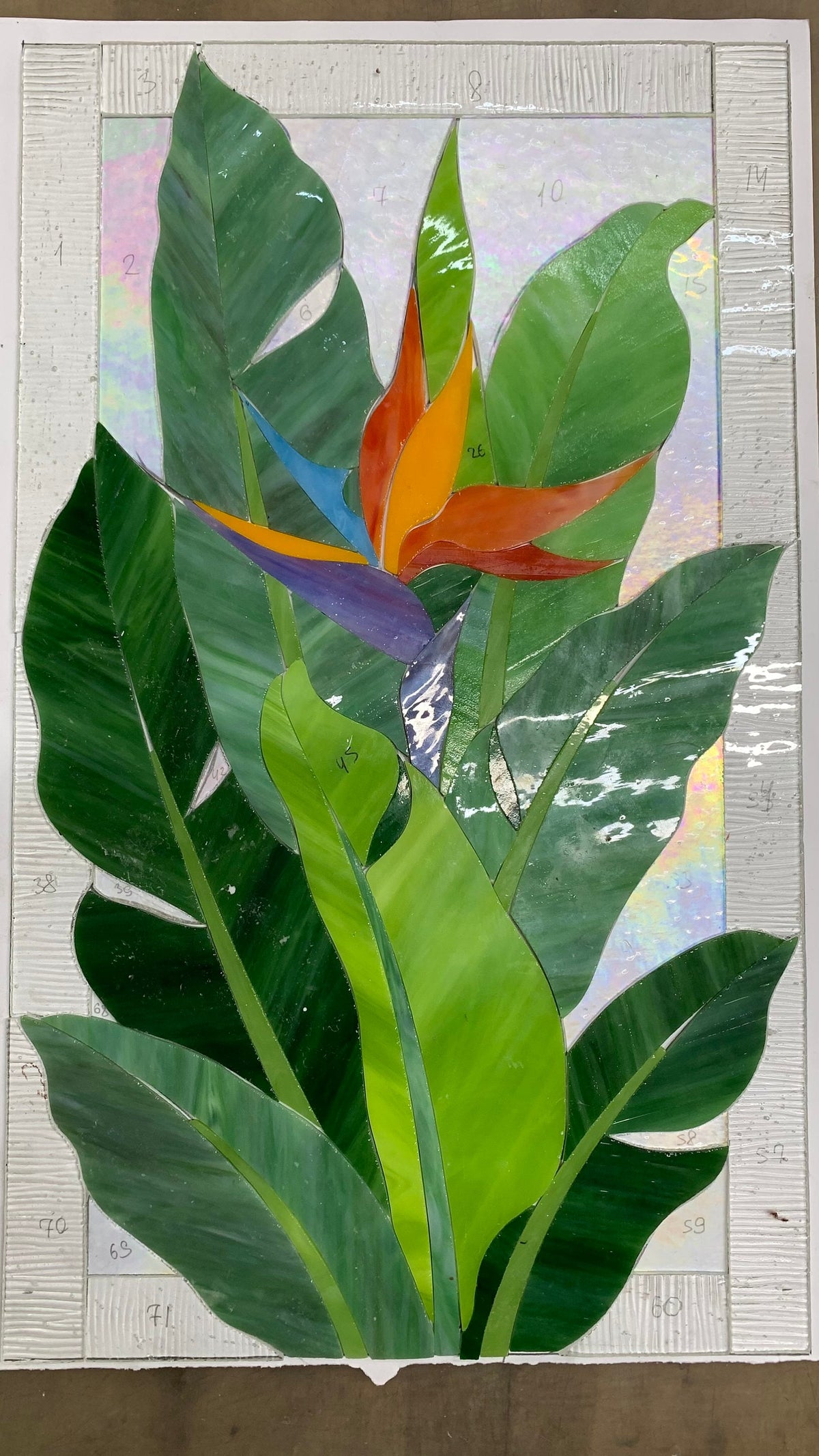 Glass pieces for handmade Bird of Paradise stained glass panel on a light table, Tiffany copper foil technique in progress