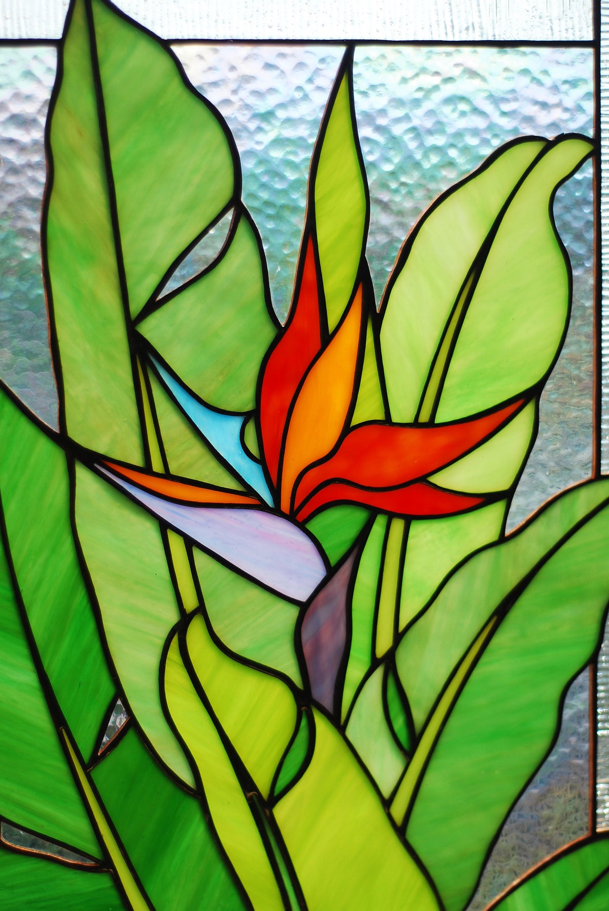 Front view of stained glass Bird of Paradise panel, vibrant orange and blue flower with rich green cathedral glass leaves