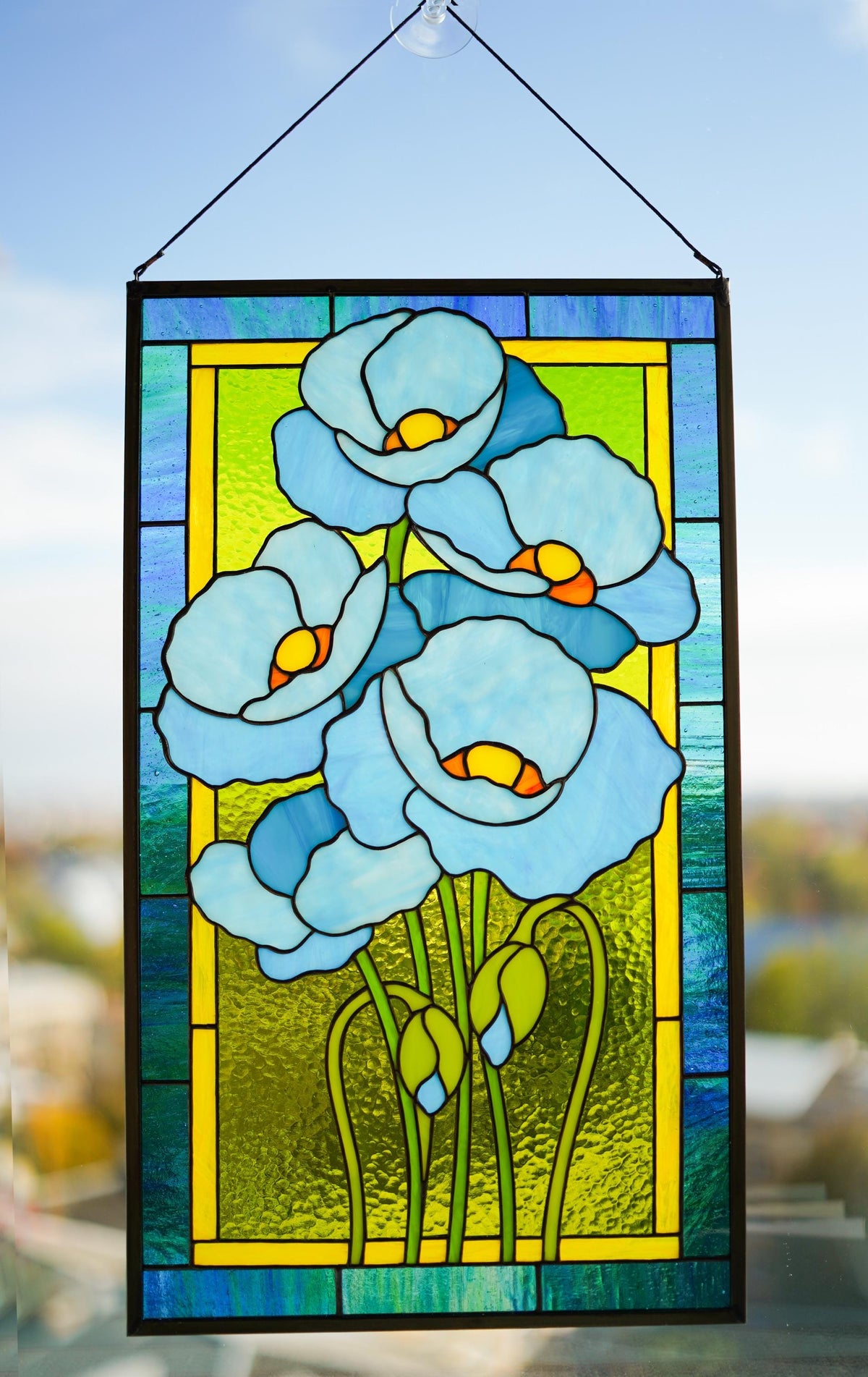 Close-up of blue poppy stained glass panel showing cathedral glass texture, copper foil lines, and yellow centre
