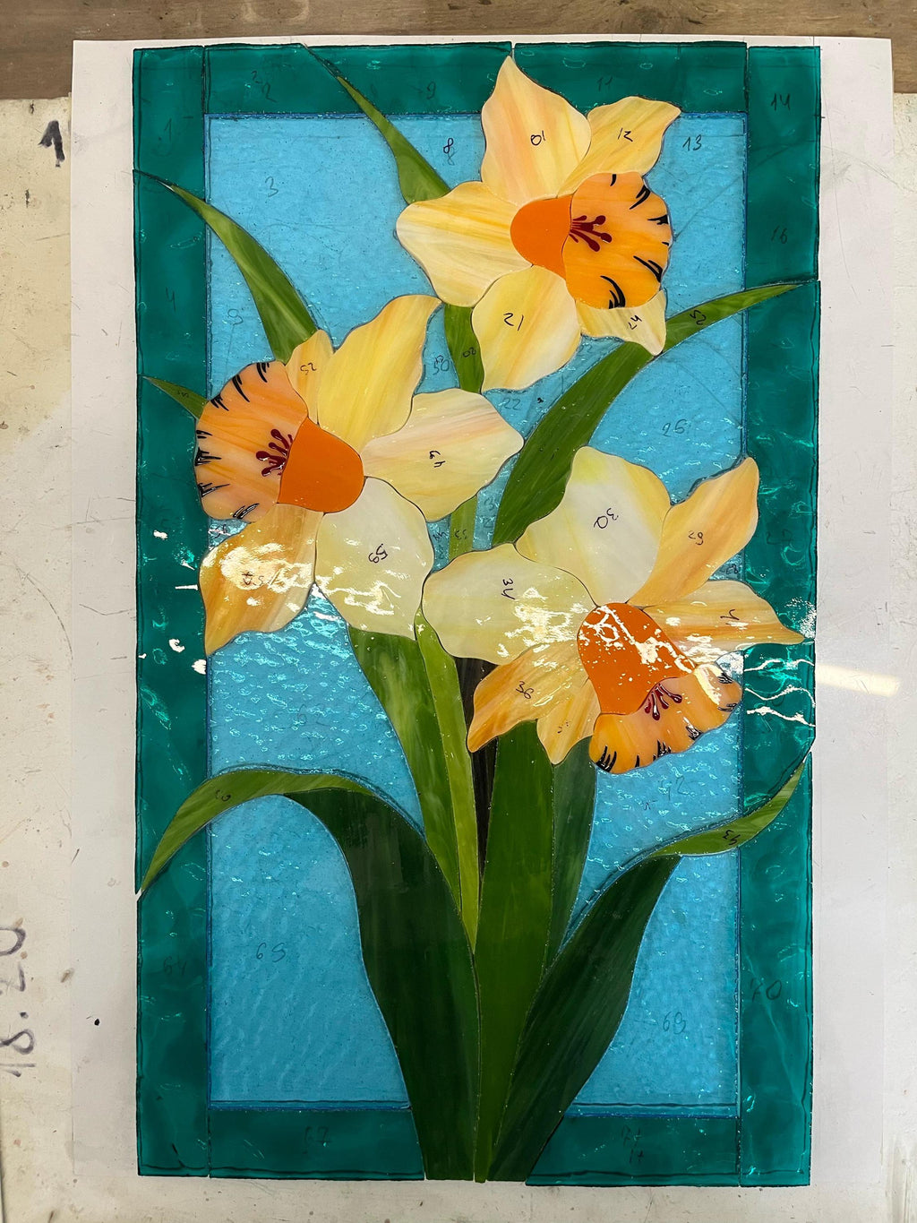 Handmade stained glass daffodil panel during assembly, yellow and green cathedral glass pieces laid out