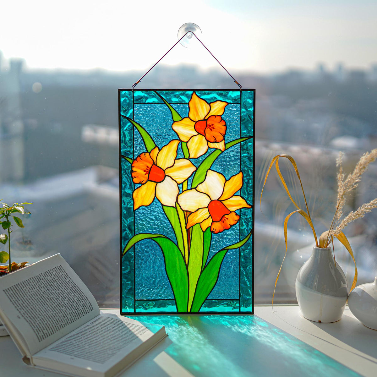Stained glass narcissus panel hanging in a bright city window, yellow and orange cathedral glass daffodils