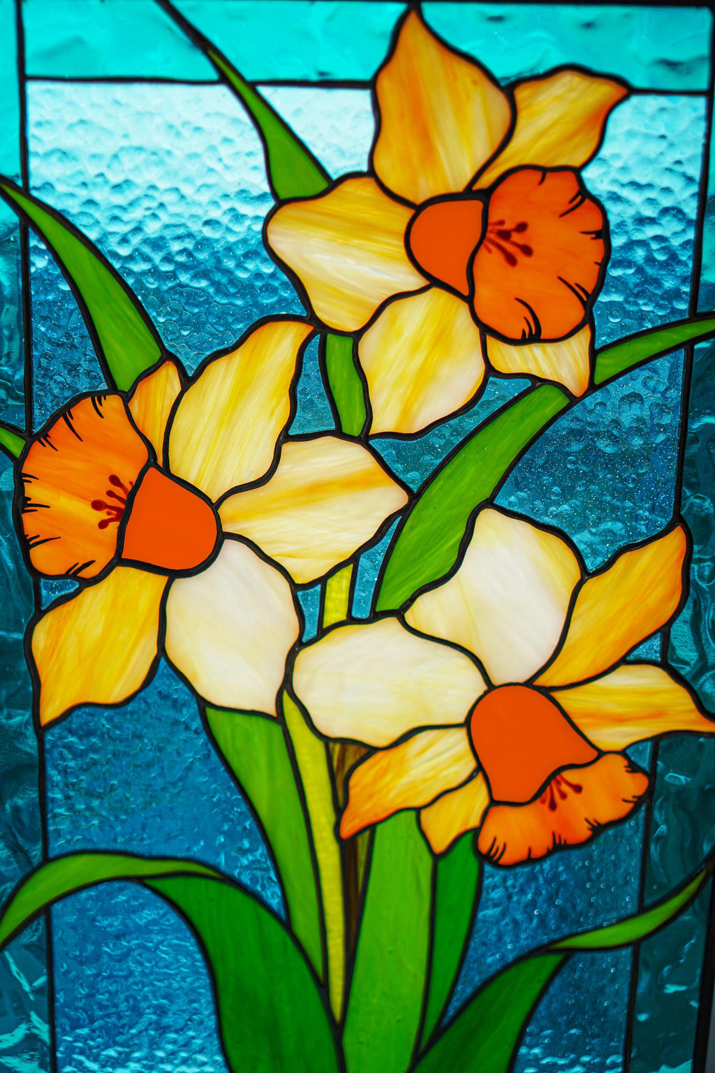 Stained glass yellow daffodil panel with orange centers and green leaves on turquoise background, Tiffany style