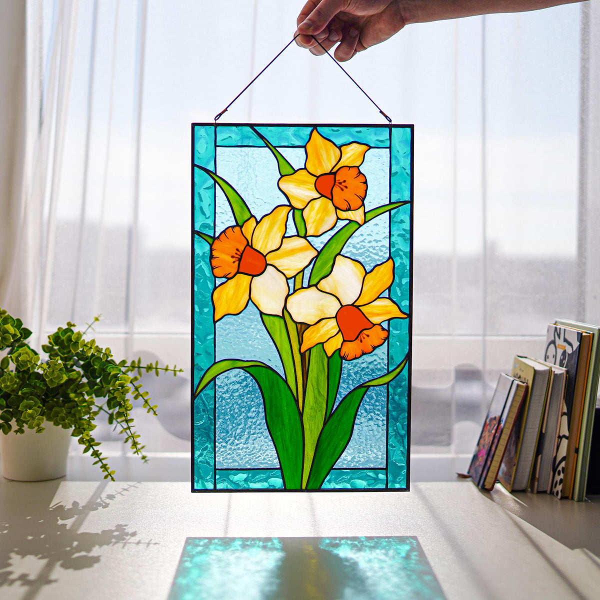 Handmade stained glass daffodil panel with yellow narcissus, held up in a sunny window, Tiffany copper foil technique
