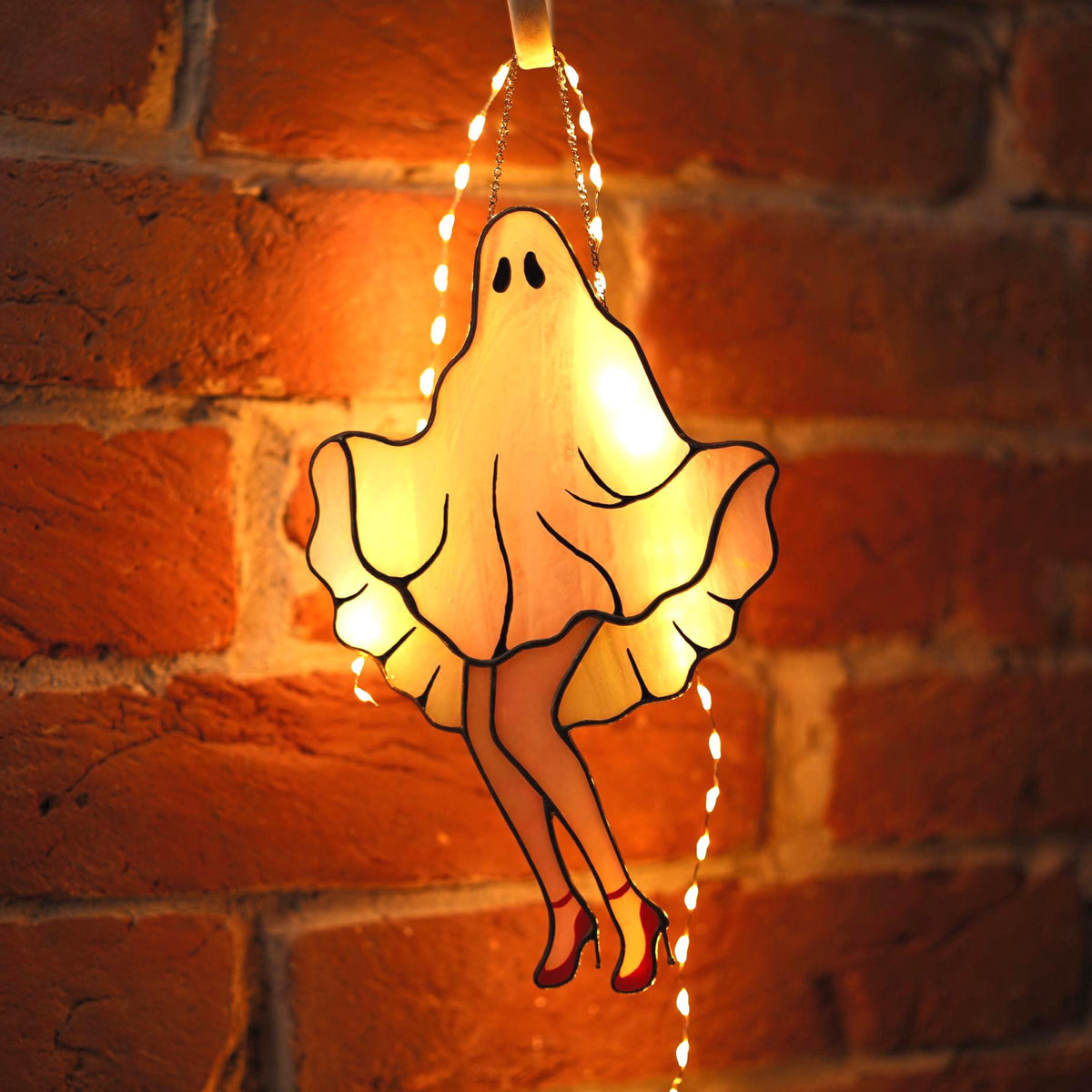 Stained glass Marilyn Monroe ghost suncatcher glowing with warm light against a brick wall