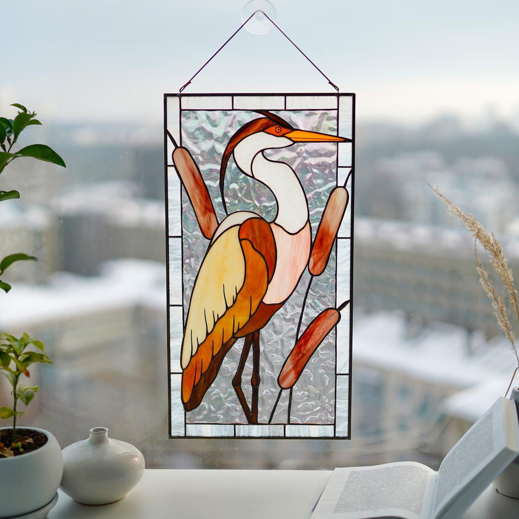 Stained glass heron with reeds panel in a bright window, warm amber and white cathedral glass