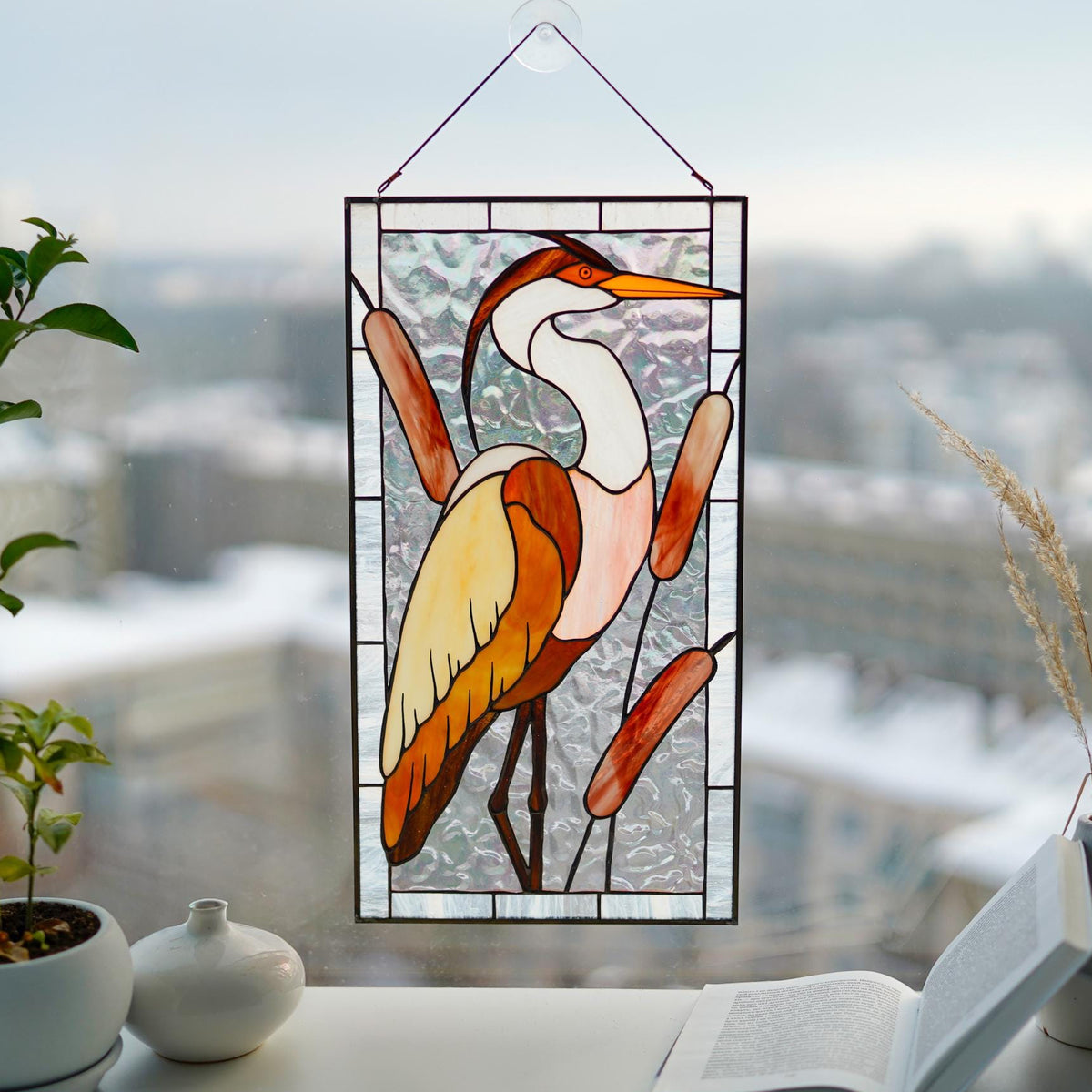 Stained glass heron with reeds panel in a bright window, warm amber and white cathedral glass
