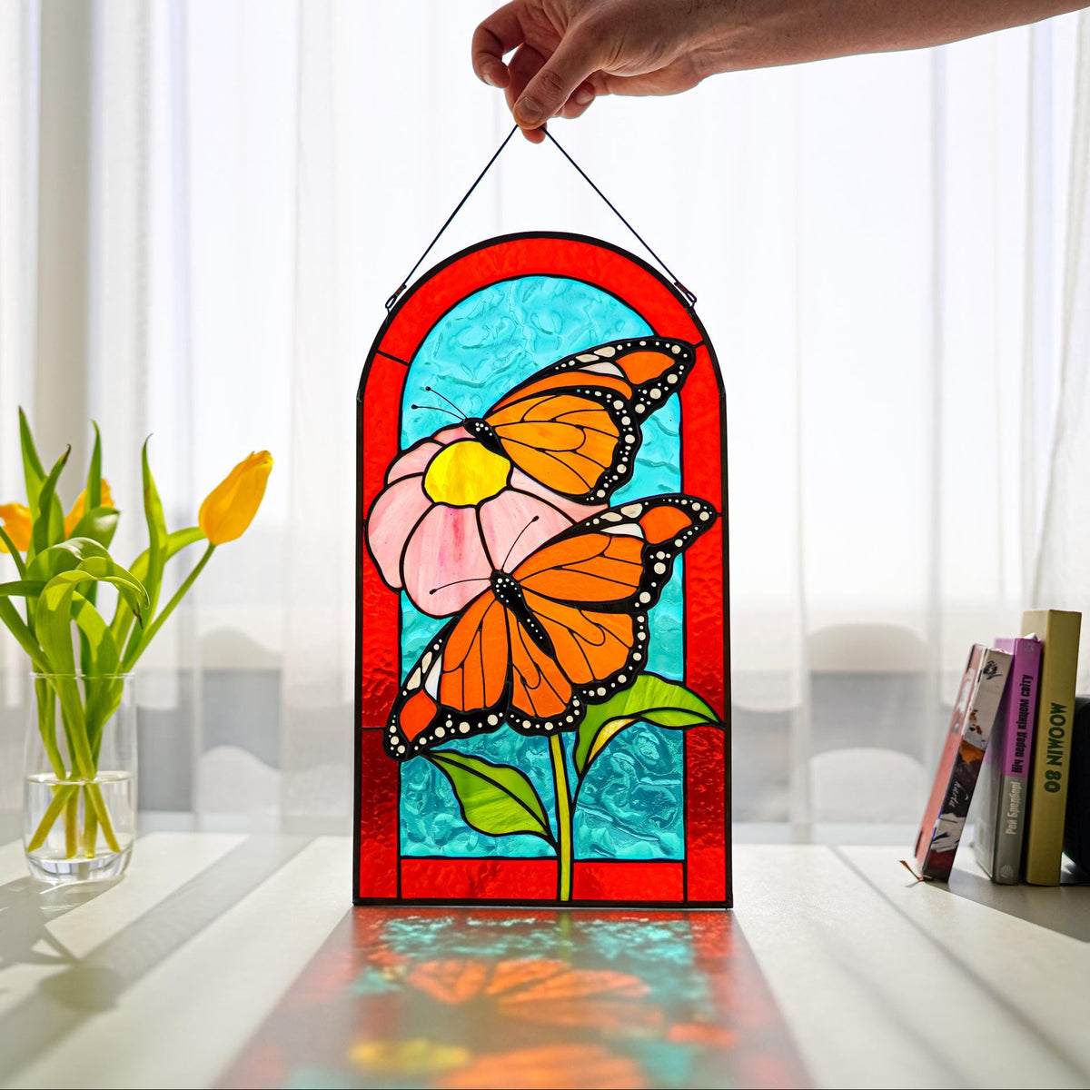 Handmade stained glass monarch butterfly panel with pink flower, held up in a sunny window, Tiffany copper foil technique