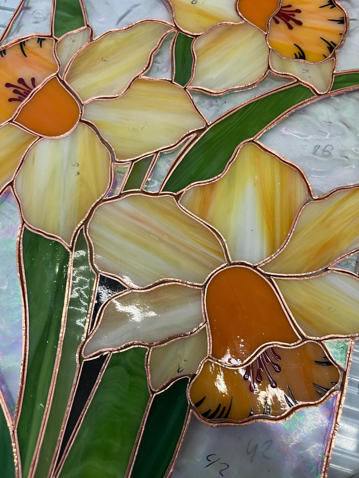 Handmade stained glass narcissus panel during assembly, yellow and green cathedral glass pieces with copper foil