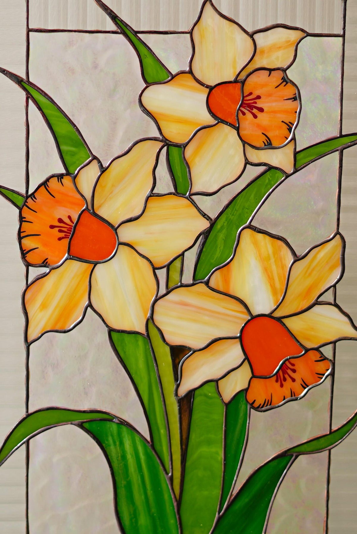 Close-up of handmade stained glass narcissus panel, vibrant yellow and orange cathedral glass daffodil petals