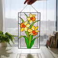 Handmade stained glass narcissus panel with three yellow orange daffodils, held up in a sunny window, Tiffany copper foil technique
