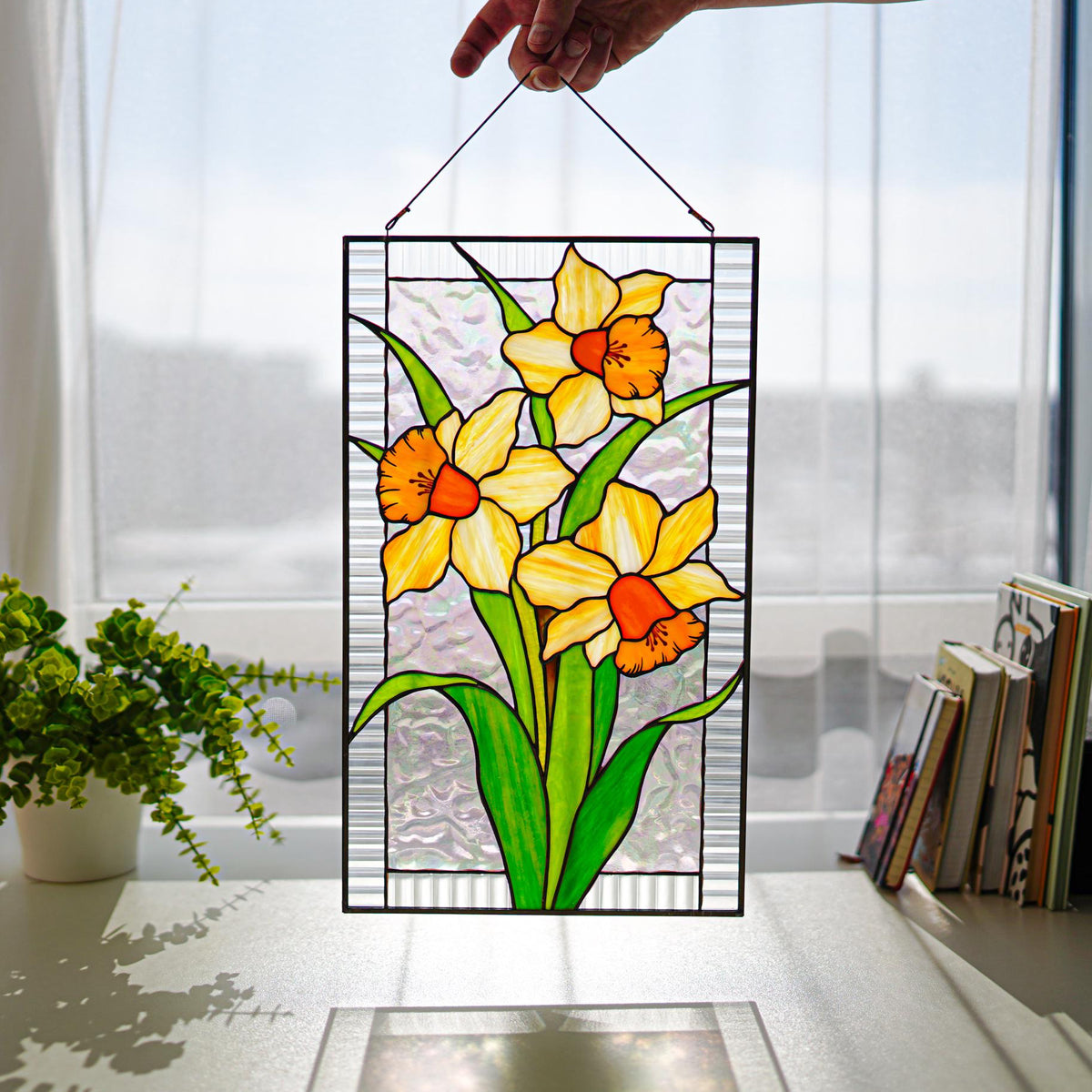 Handmade stained glass narcissus panel with three yellow orange daffodils, held up in a sunny window, Tiffany copper foil technique