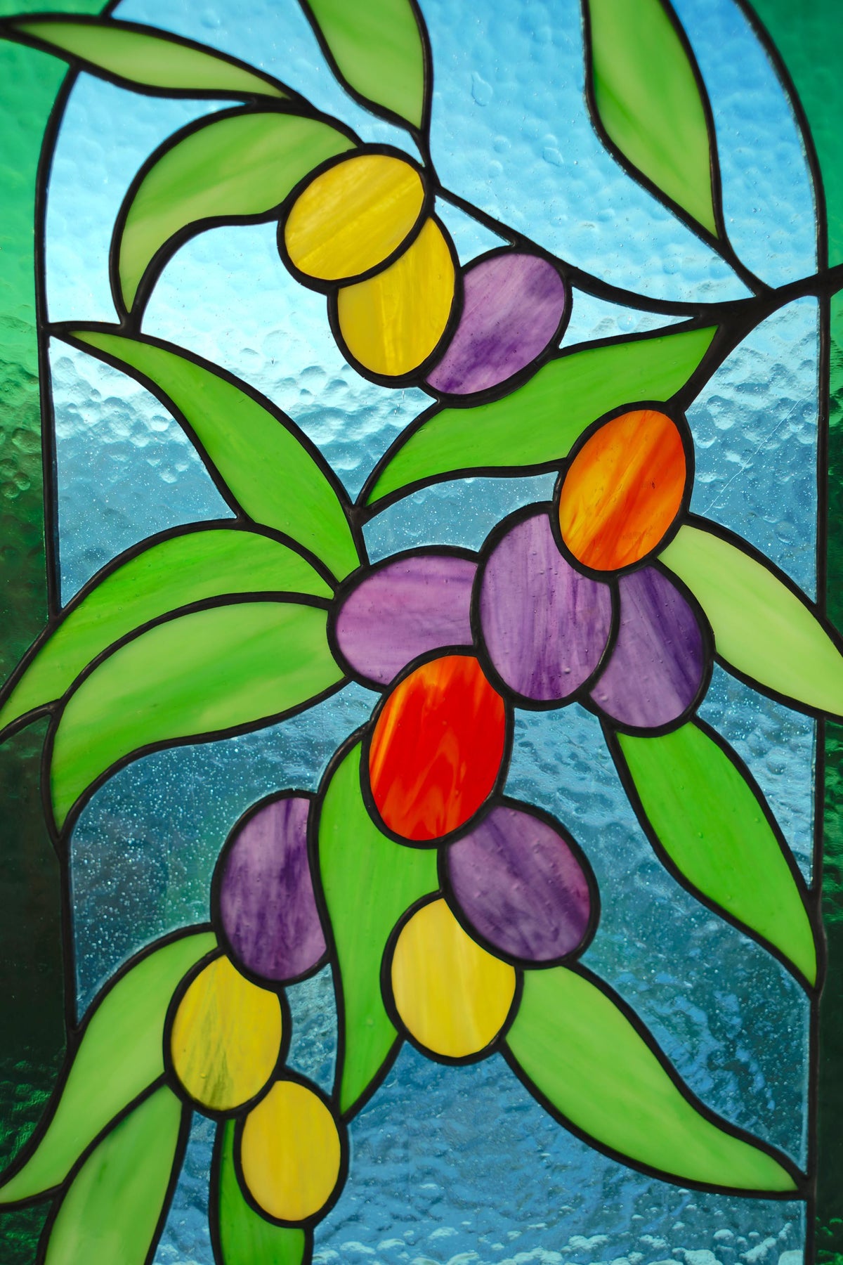 Close-up of handmade stained glass olive branch, vibrant green yellow red and purple cathedral glass olives