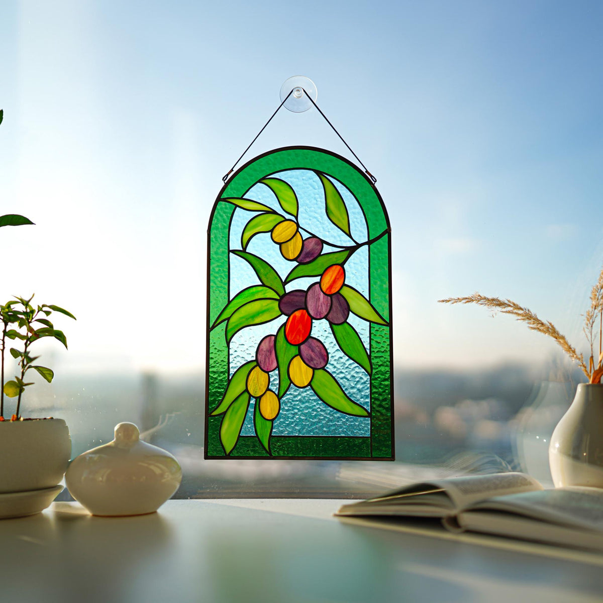 Stained glass olive branch arched panel in a sunny window with indoor plant, Mediterranean botanical decor