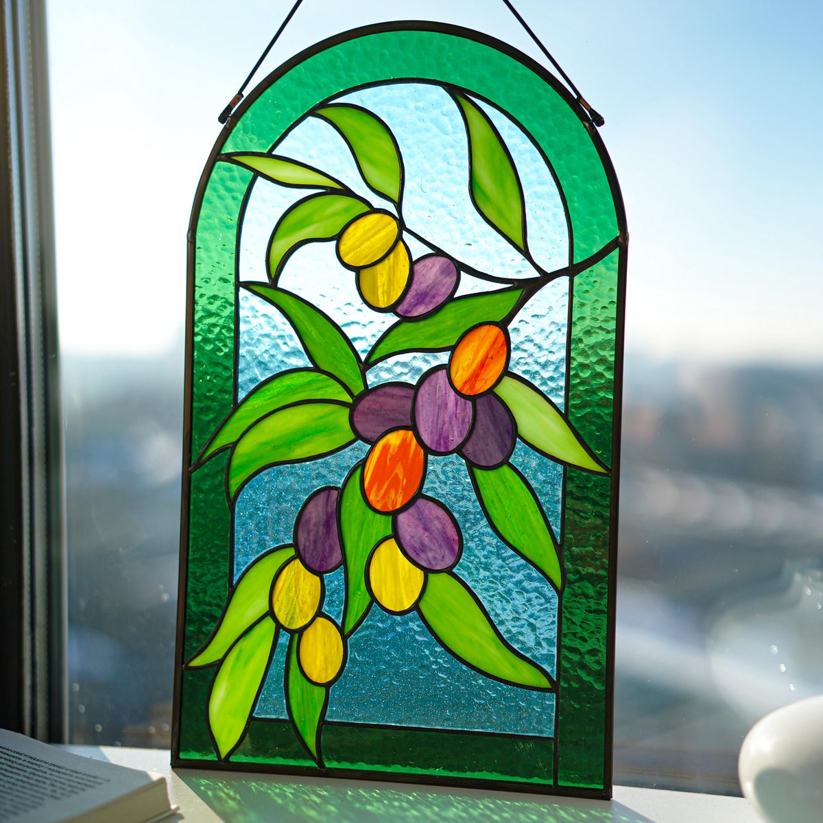Stained glass olive branch panel hanging in a bright window, green arch frame, Tiffany copper foil method