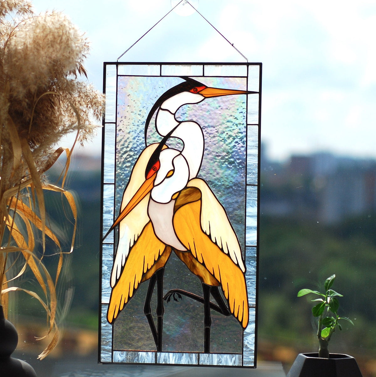Stained glass pair of herons panel displayed on a windowsill with dried flowers and nature backdrop