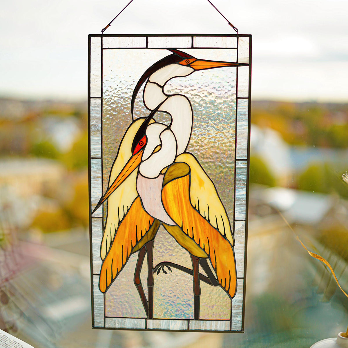 Stained glass two herons panel hanging in a bright window, warm amber and white glass, Tiffany style