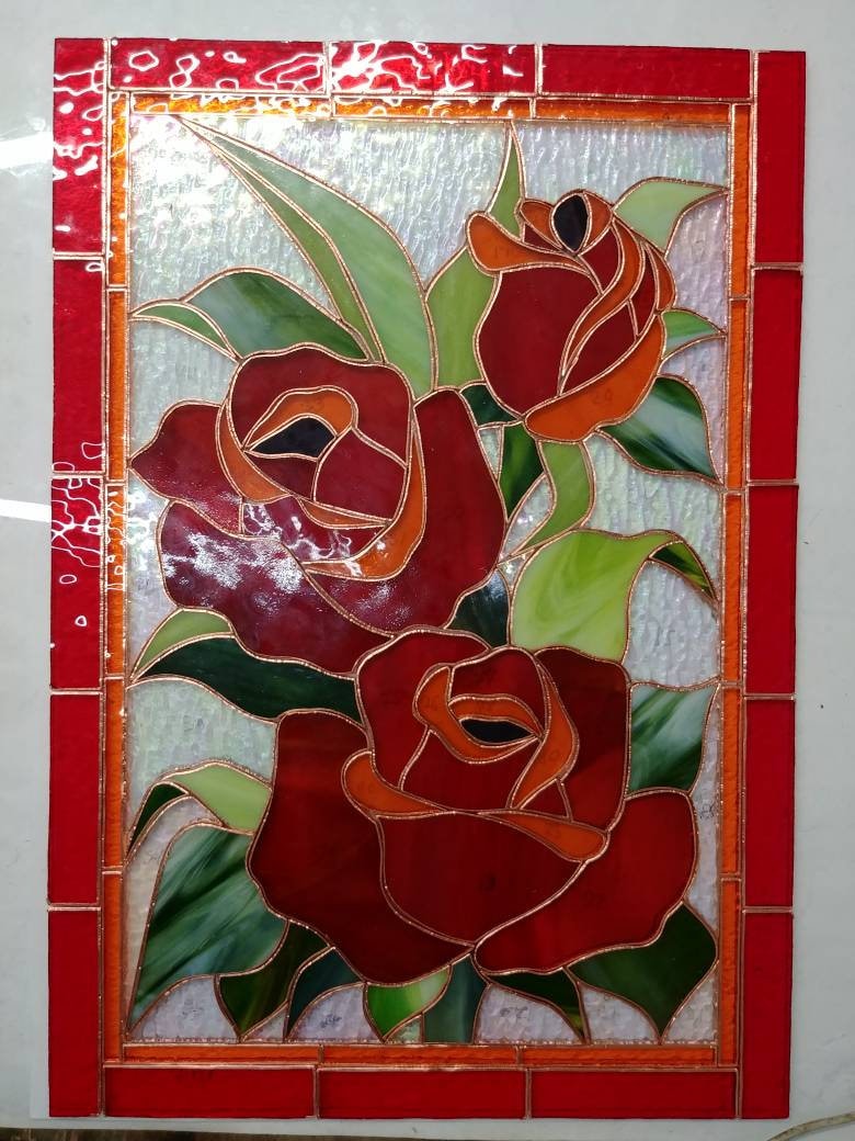 Handmade stained glass red rose panel during assembly, red cathedral glass pieces with copper foil