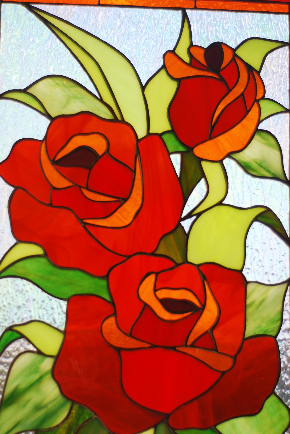 Close-up of handmade stained glass red roses panel, vibrant red cathedral glass petals and green leaves