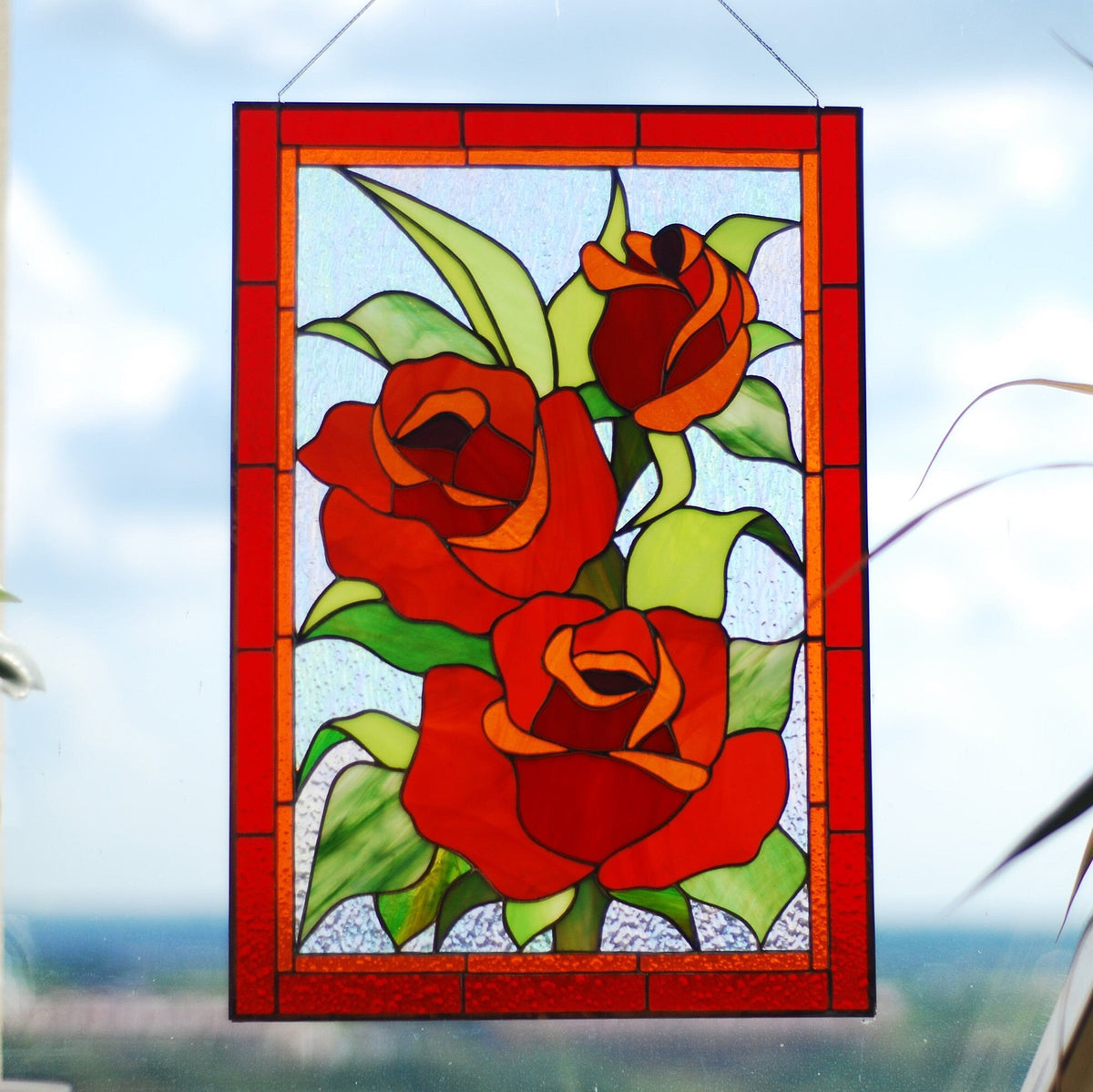 Handmade stained glass red rose panel with three roses and green leaves, hanging outdoors, Tiffany copper foil technique