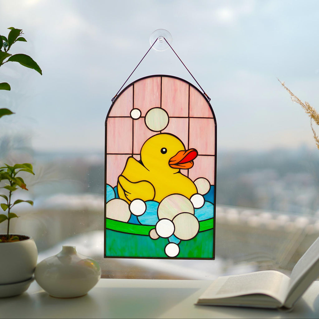 Stained glass rubber duck panel with colorful cathedral glass, hanging in a bright window