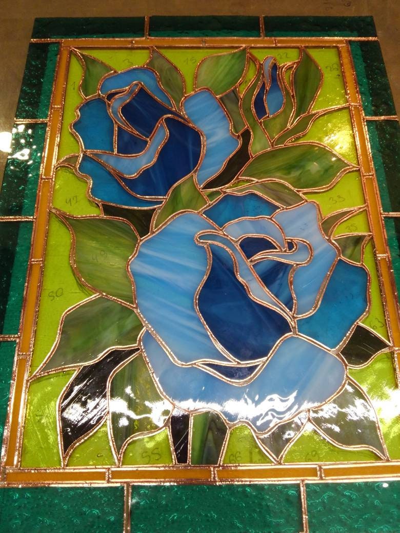 Stained glass blue rose panel work in progress on a light table, blue and teal glass pieces with copper foil technique, handmade process
