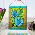 Handmade stained glass blue rose panel held up in a bright window, turquoise and teal roses with green leaves, Tiffany copper foil, 11x14 inches
