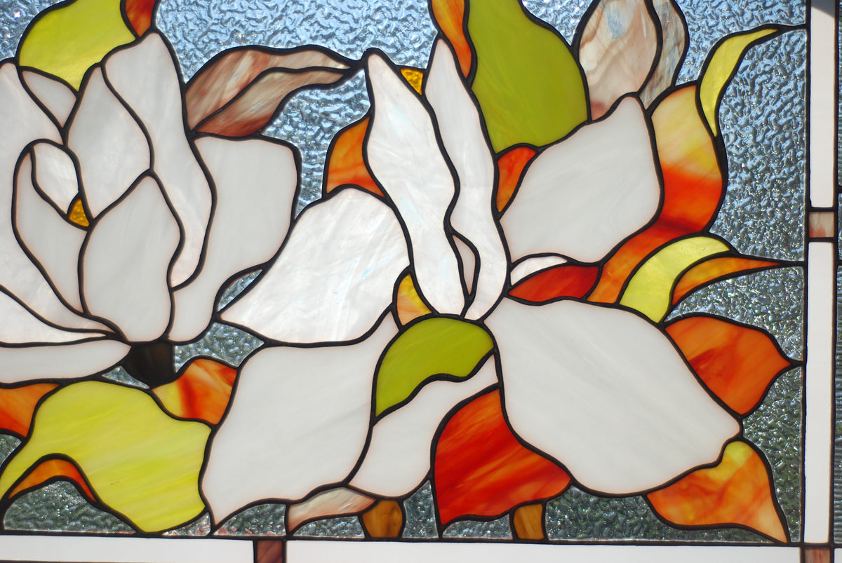 Close-up of handcrafted stained glass magnolia blossom, white and cream glass petals with copper foil detail, floral window hanging
