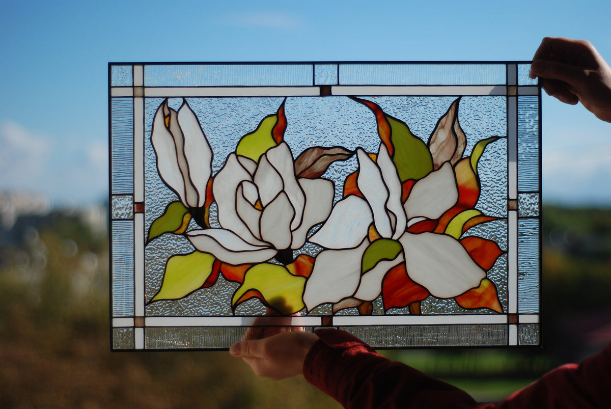 Stained glass magnolia panel backlit by natural sunlight, translucent white cathedral glass petals glowing, handmade window art

