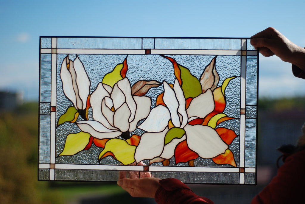 Stained glass magnolia panel with zinc frame detail, held up against natural light outdoors, spring floral window hanging
