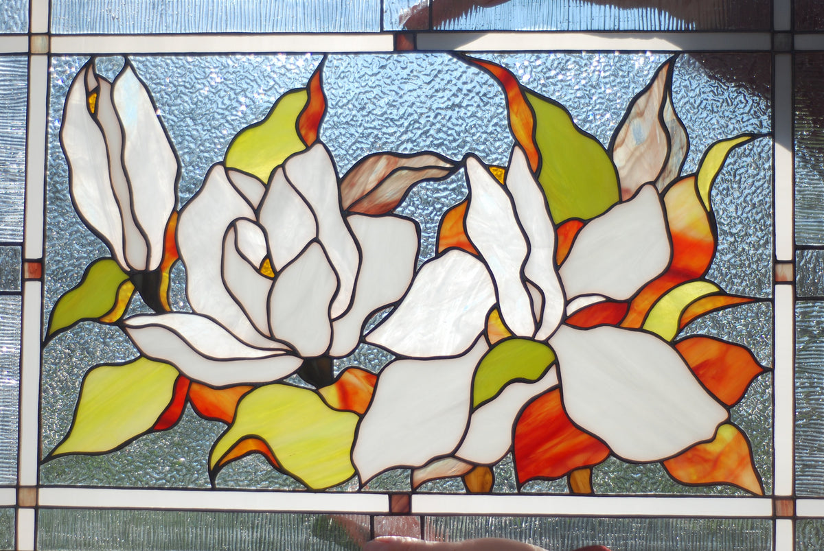 Stained glass magnolia window panel front view, white and cream petals with vivid orange and green foliage, handmade Tiffany style floral art
