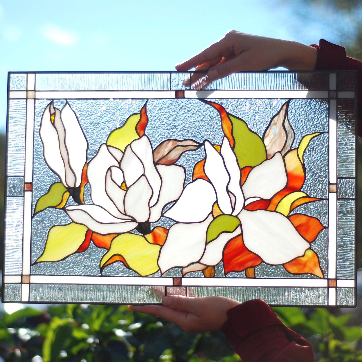 Handmade stained glass magnolia panel held outdoors, white magnolia blossoms with orange and green leaves, Tiffany copper foil, 16x11 inches
