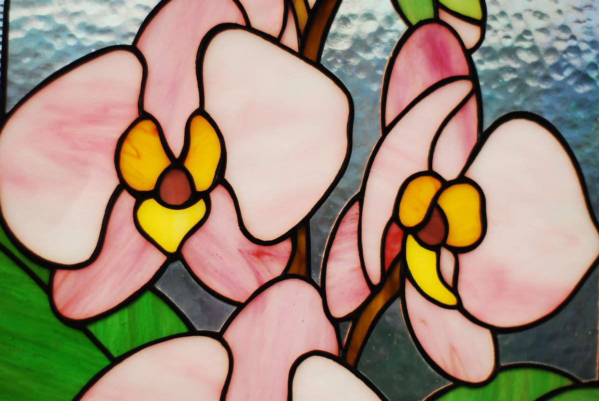 Close-up detail of handcrafted stained glass orchid blossoms, soft pink cathedral glass petals with yellow centres and copper foil soldering
