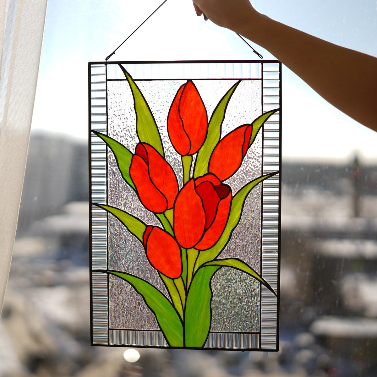 Handmade stained glass red tulip window hanging held in sunlit window, four blooms with green leaves, textured clear glass, Tiffany copper foil art
