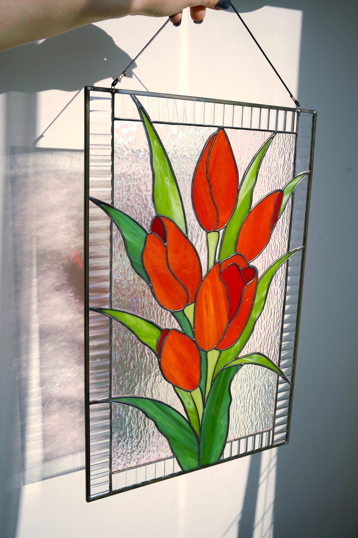 Stained glass red tulip floral panel held sideways showing zinc frame and copper foil detail, vivid red and green cathedral glass, handmade Ukraine
