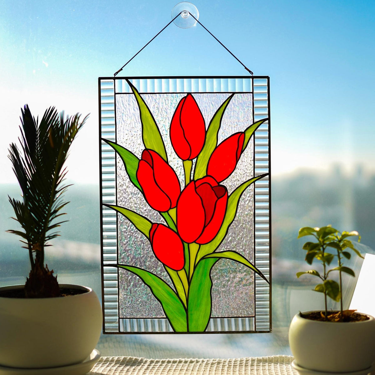 Stained glass red tulip panel on windowsill with plants and books, four bold red blooms on textured clear background, Tiffany style, 16x10.5 in
