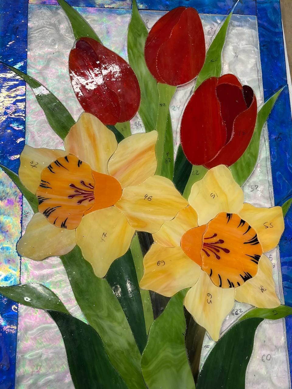 Stained glass tulips and daffodils close-up during production, red and yellow cathedral glass, Tiffany method